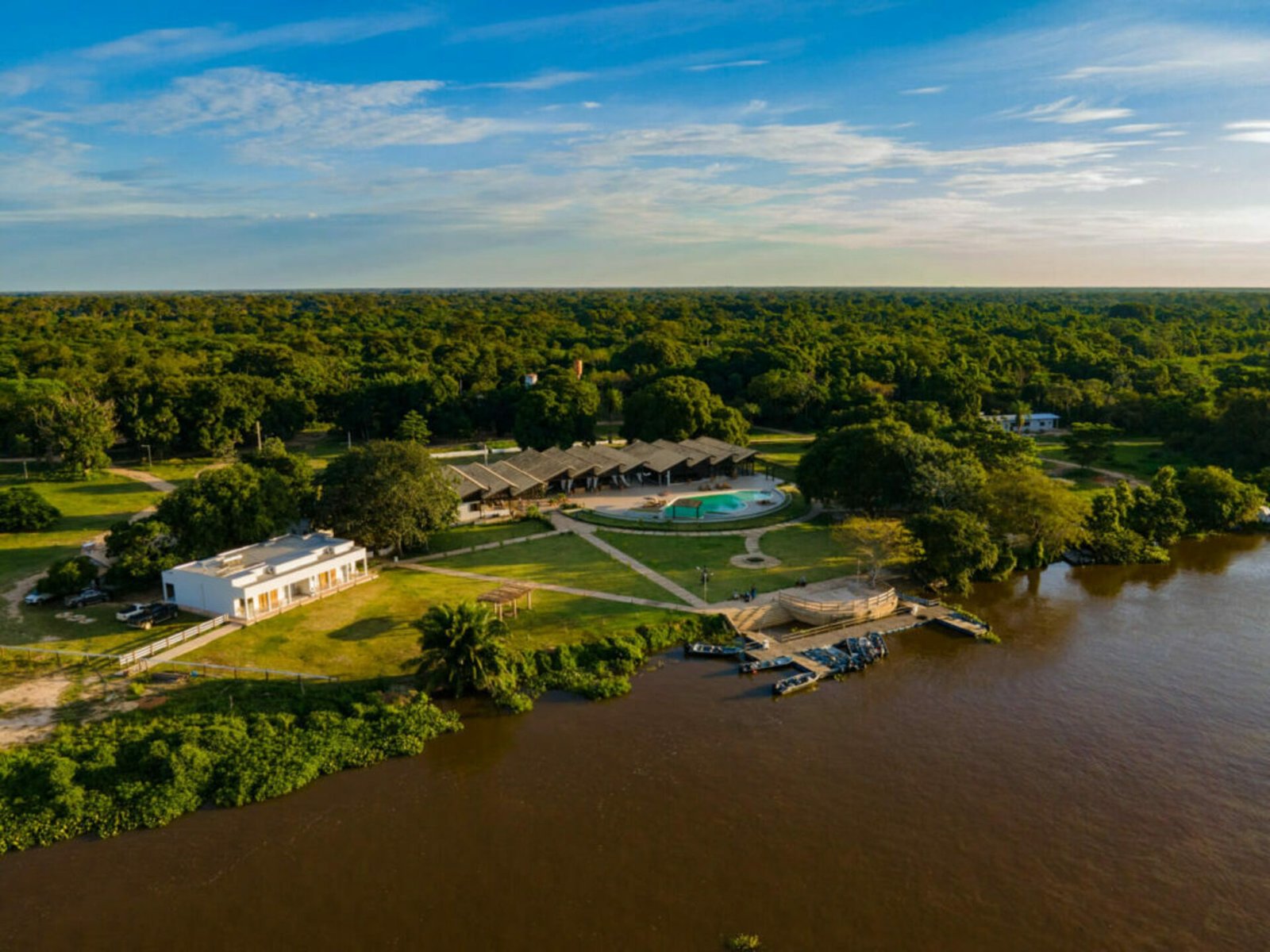 Aerial view of Santa Rosa Pantanal Hotel on the riverbank, with the pool, lawns, the pier and boats, surrounded by forest