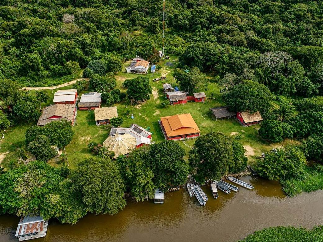 Aerial view of SouthWild Porto Jofre Pantanal Lodge, with red-roofed buildings among forest beside the river and boats moored along the bank