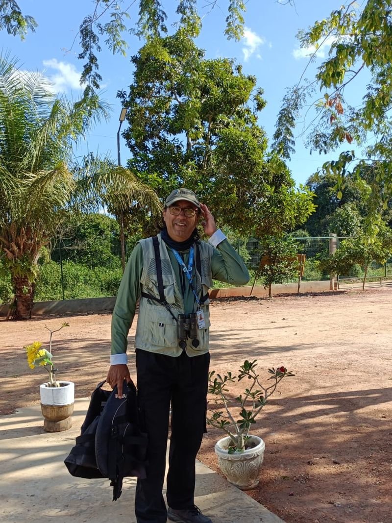 José de Andrade, known as Zé Cabelinho, a guide wearing a field vest and binoculars, standing among trees and palms in the Pantanal