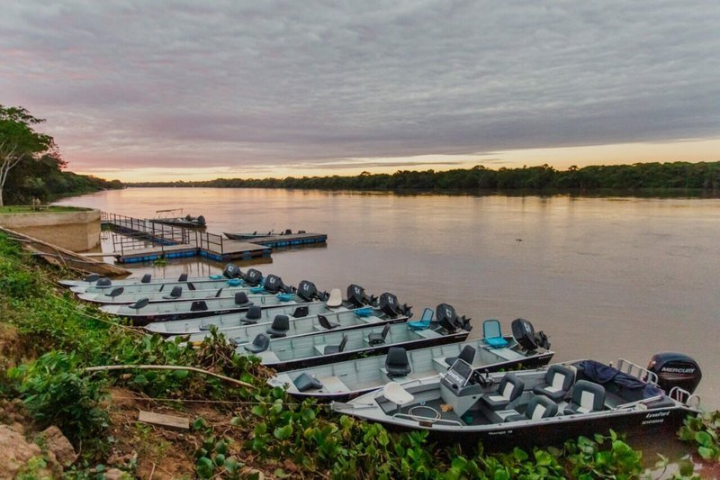 Aluminum boats moored on the riverbank beside a floating pier, under a cloudy sky