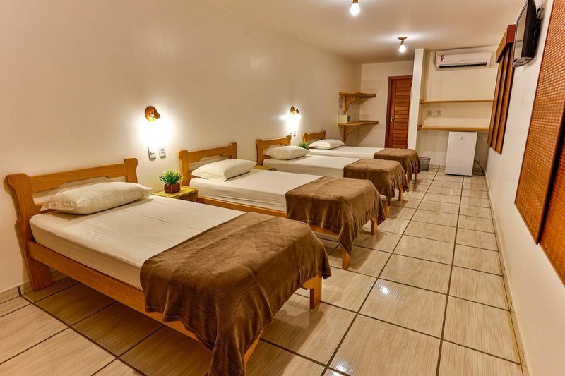 Apartment with four single beds with brown throws, an air conditioner, a wall-mounted TV, wooden shelves and a minibar