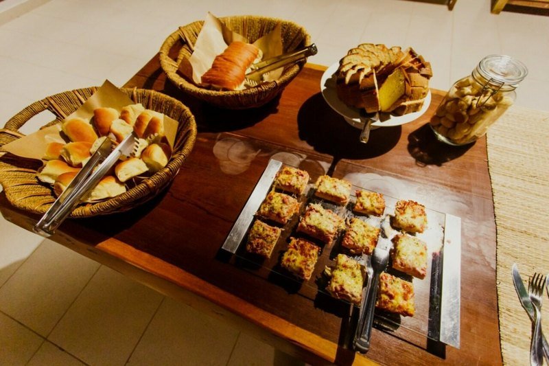 Baskets of bread rolls, sliced cake, a jar of biscuits and a tray of baked savory squares on a wooden table