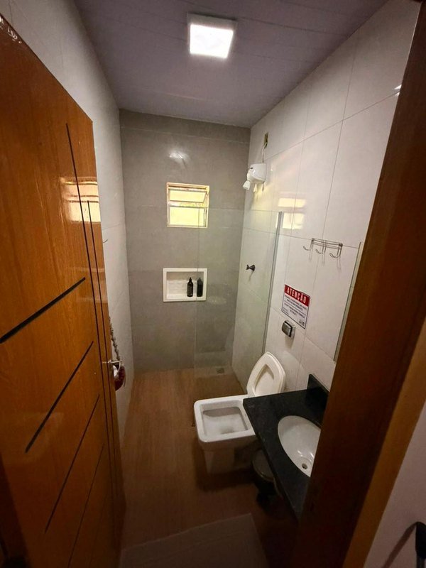 Bathroom with a glass shower screen, an electric shower, a toilet and a sink on a dark counter