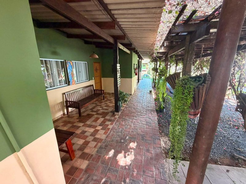 Covered veranda with green walls, wooden benches and a brick walkway beside a garden with hanging plants