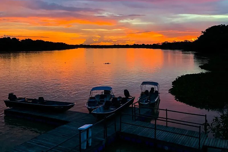 Boats at the floating pier with an orange and pink sunset reflected on the river