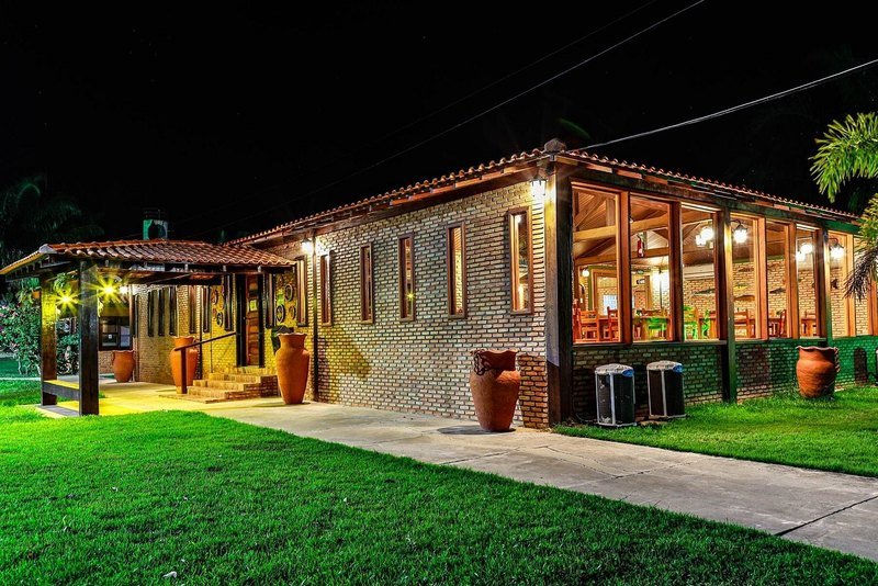 Brick building with large lit windows and a tiled roof at night, with clay vases along the path and a lawn in front