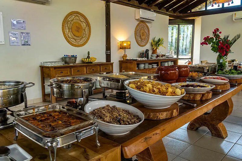 Buffet on a long wooden table with hot dishes, salads, clay pots and a vase of red flowers