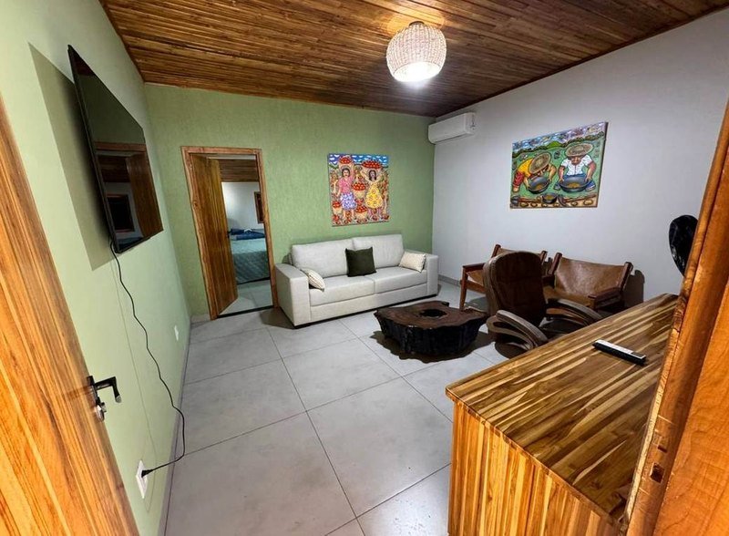 Living room with a sofa, armchairs, a wooden coffee table, a wall-mounted TV and colorful paintings