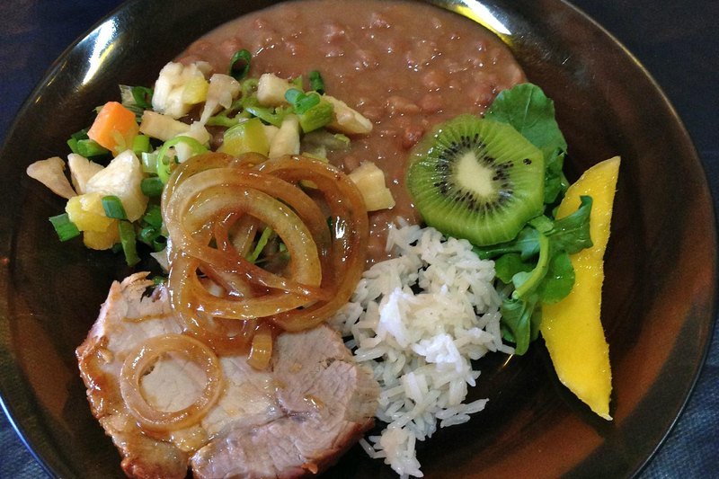 Plate with roast pork and onions, rice, beans, vegetable salad, watercress, kiwi and mango