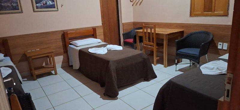 Room with single beds with brown covers and folded towels, a wooden table, chairs and wood-panelled walls