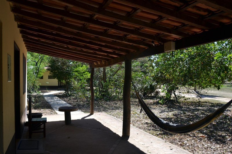 Covered veranda with a tiled roof, a hammock, a wooden bench and a small table, facing the trees
