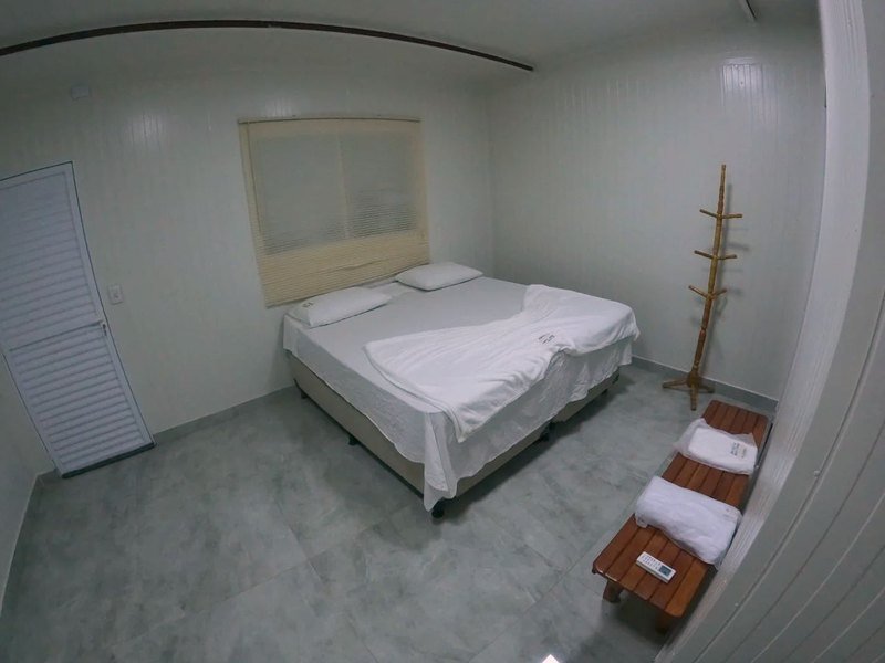 Room with a double bed, a window with blinds, a coat stand and a wooden bench with towels