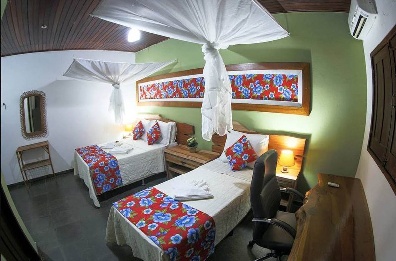 Room with two beds with red and blue floral runners, mosquito nets, wooden headboards and a desk