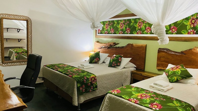 The same room seen from the desk, with a wicker-framed mirror, an office chair and two beds with green floral runners