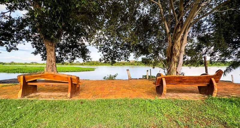 Two carved wooden benches under trees, facing the river